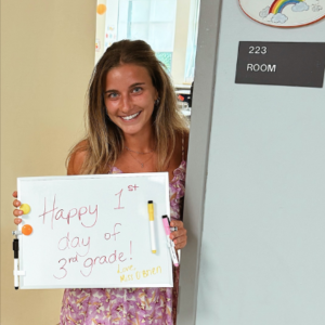 Photo of Julia O'Brien as she holds up a sign stating "Happy 1st Day of 3rd Grade!"