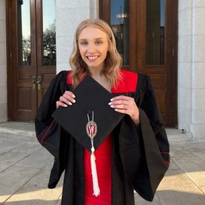 Claire Bowman wearing a graduation gown, holding her cap with the University of Wisconsin logo.