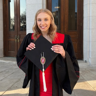 Claire Bowman wearing a graduation gown, holding her cap with the University of Wisconsin logo.